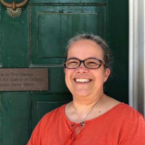 Smiling Woman wearing glasses and an orange shirt standing in from of a green door